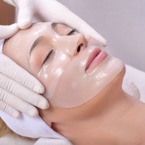 Young female getting skin mask treatment on her face with massage glove A young female getting skin mask treatment on her face with massage glove